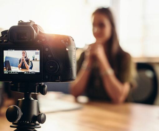 Video camera on a flexible tripod recording a woman sitting at a desk.