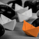 orange paper boat leading others through rocks